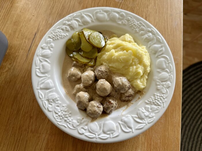 Tallrik med köttbullar i gräddsås, potatismos och skivad inlagd gurka.