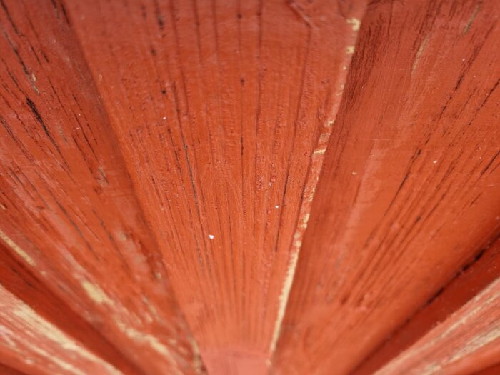 Röd träfasad med smala lockläktstumlingar och synligt träkorn, fokus på ytan och strukturen.