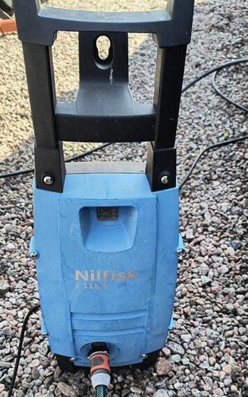 Blå Nilfisk högtryckstvätt på grusgång, med sladd och slang anslutna.