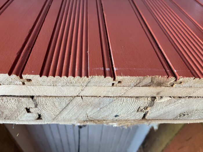 Röd träpanel med räfflat mönster, staplad på varandra, använd för ytterväggar i äldre hus.