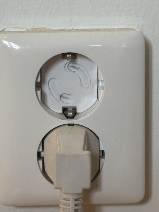 Vägguttag med petskydd och inkopplad kontakt, petskyddet saknar verktyg för att avlägsnas.