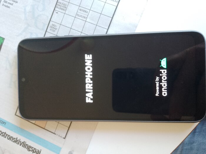 Fairphone med Android-logotyp på skärmen ligger horisontellt på ett bord.
