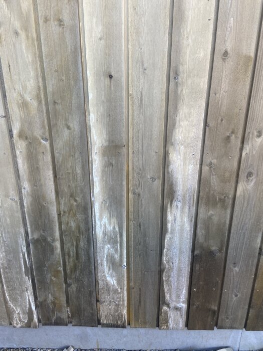 Missfärgad träpanel med vitaktiga fläckar, oregelbundet spridda över ytan, möjliga att åtgärda med högtryckstvätt eller fasadtvätt.