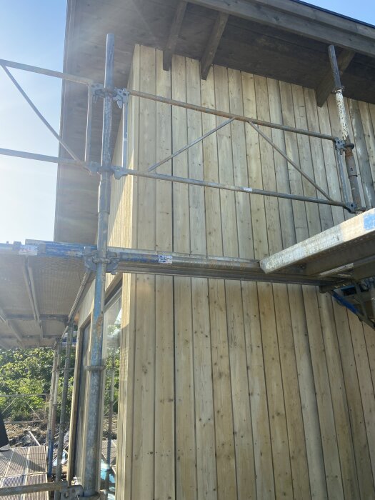 Fasad med träpanel och byggställning, synlig missfärgning på panelen.