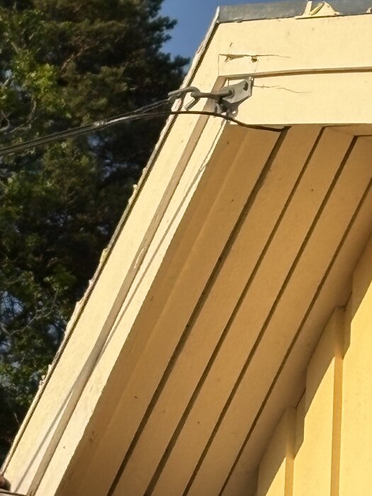 Vajer som håller kopparkabel monterad i en vindskiva på en byggnad, omgiven av träd i bakgrunden.