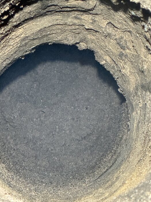 En närbild av ett borrat hål i marken, med steniga och ojämna sidoväggar, där borren nått en hård yta.