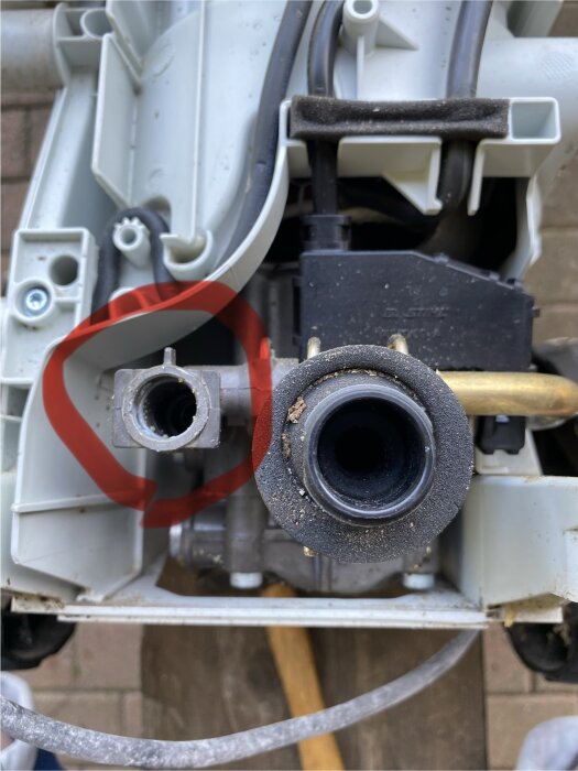 Delar av en maskin med avlägsnade kåpor, synliga ventiler och kablar; en röd cirkel markerar en specifik del bredvid en öppning.