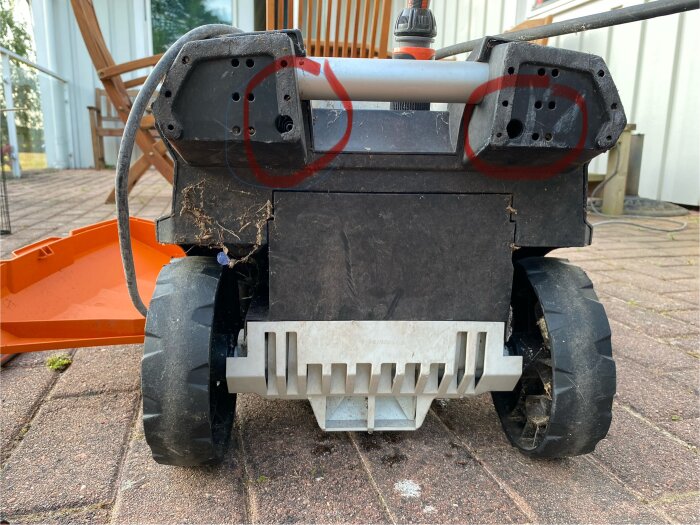 Bild på en arbete med en trädgårdsmaskin där skyddskåpor tagits bort. Två runda markeringar syns på den övre delen av maskinen.