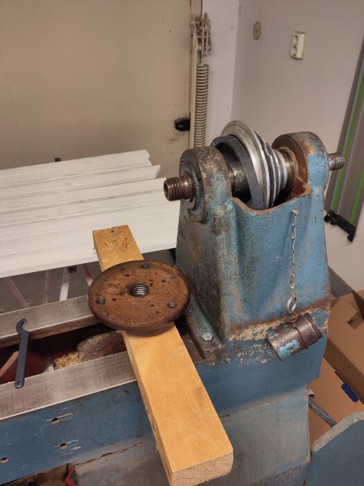 En metallkomponent är lossad från en maskin med hjälp av en träbit och diverse verktyg i en verkstadsmiljö.