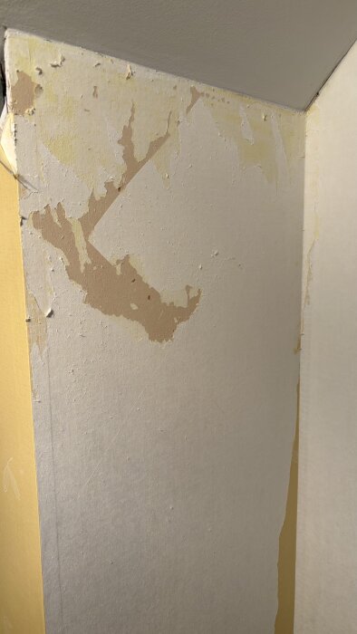 Vägg med avskalad tapet där endast rester och lim är kvar, visar ojämt och fläckigt underlag efter att ha försökt ta bort gammal tapet.