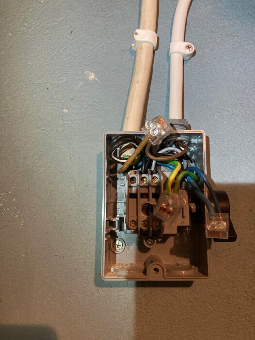 Elkabelskarvning i en grå kopplingsbox med synliga ledare och kontaktklämmor, monterad vid en svagt färgad vägg.