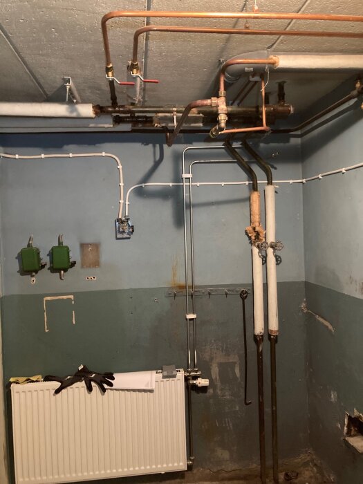 Gammal elektrisk installation i ett rum med synliga kopparrör och radiator, kablar löper längs väggen. Potentiella risker med eldragningar diskuteras.