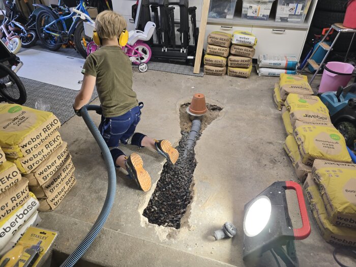 Barn dammsuger betonggolv vid gjutning i garage; betongsäckar och byggverktyg synliga.