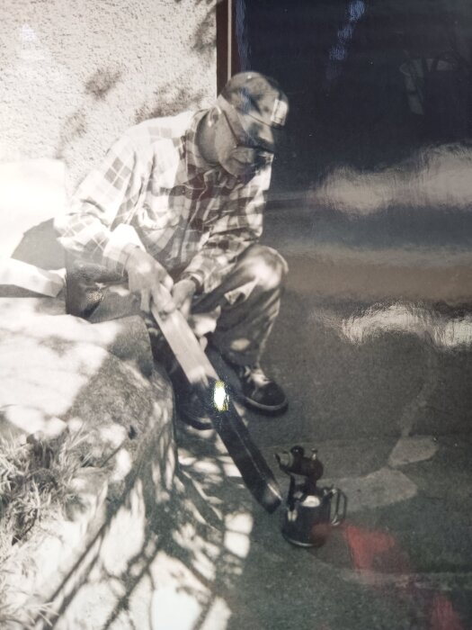 Äldre man använder blåslampa för att kola trästolpe i solen.