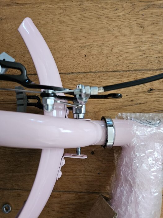 Rosa cykelram sett ovanifrån med en omonterad stänkskärm och synlig skruv som är för kort för att nå skärmen, mot bakgrund av ett trägolv.