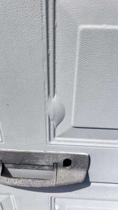 Färgen på en äldre garageport som bubblar och flagnar närbild vid handtag.