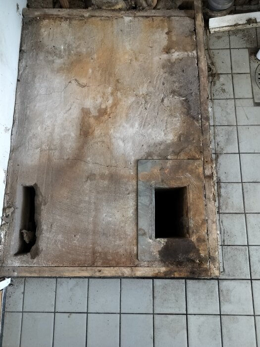 Betongplatta med två hål där en oljepanna stod, omgiven av golvplattor.