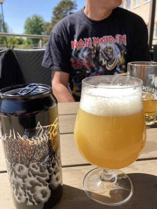 En burk och ett glas med Omnipollo-öl, samt en person i Iron Maiden-tröja på en uteservering.