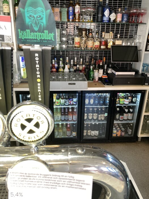Ölkranar märkta "Källartrollet" och "Rotator Series" på en bar med spritflaskor och ölfyllda kylskåp i bakgrunden.