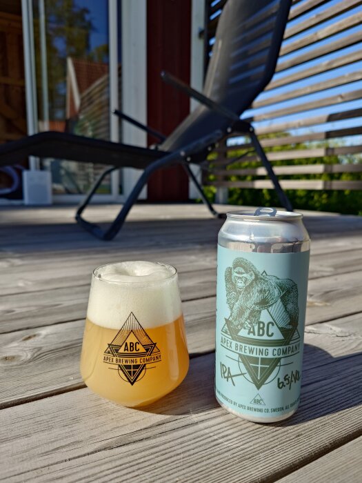 Glas och burk med Apex Brewing Company IPA på en altan, solstol i bakgrunden.