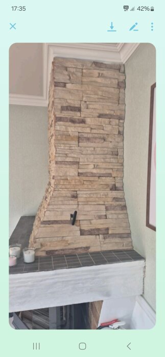 Murstock med öppen spis och påsatt kamin; några stenar är löst monterade, och det ser ut som vit puts under.