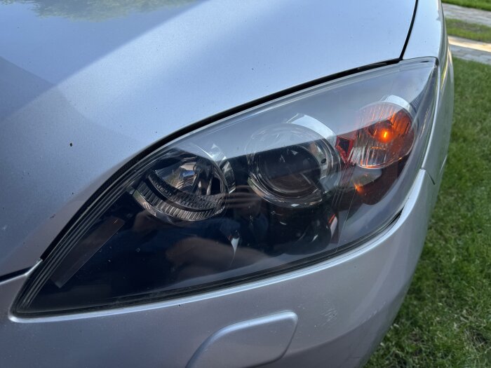 Polerad bilstrålkastare i närbild med klart glas och synlig belysning, del av ett bilvårdsprojekt med improviserade verktyg.