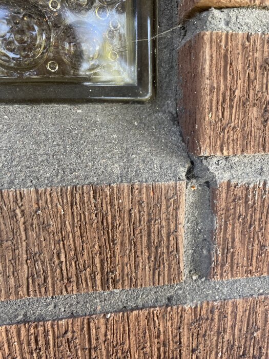 Sprucken tegelvägg med synliga fogar och ett glasblock infällt i fasaden.
