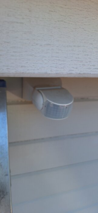 En rörelsedetektor monterad på en trävägg under ett tak.