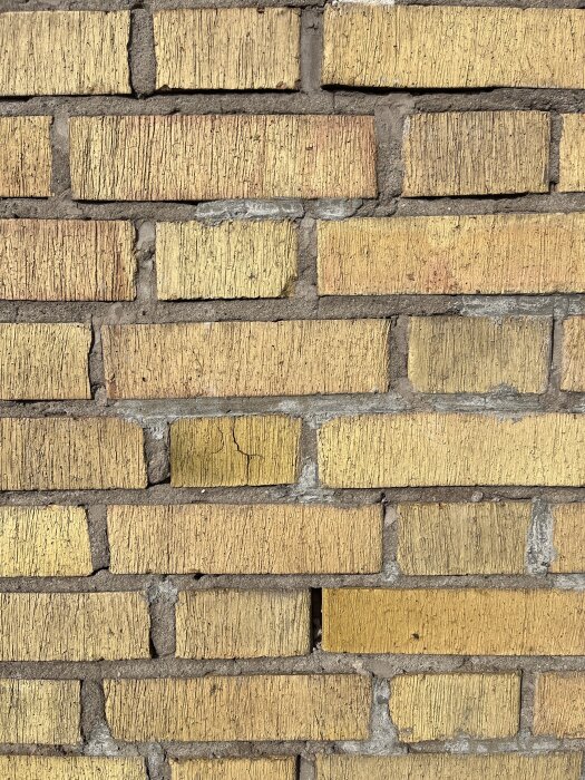 Gul tegelvägg med fogar som syns tydligt. Vissa tegelstenar har sprickor, och fogarna är ojämna.