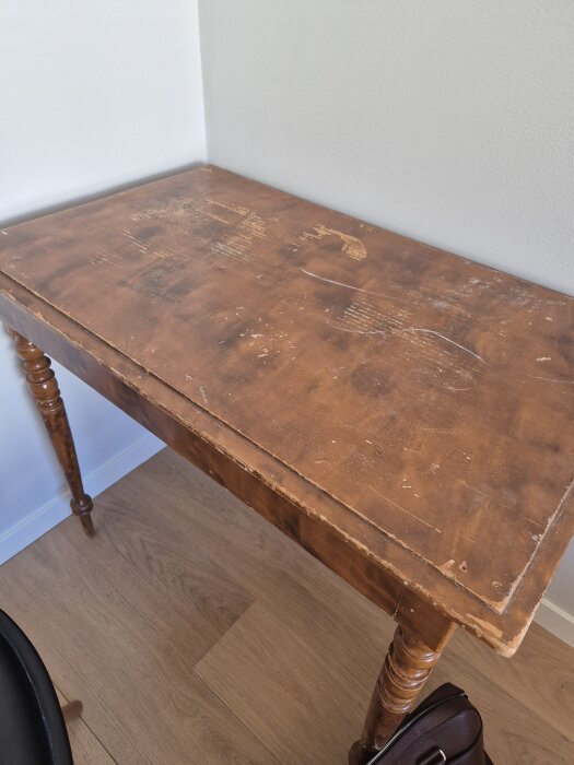 Gammalt bord med repor och slitna kanter, stående vid en vägg, med dekorativa ben.