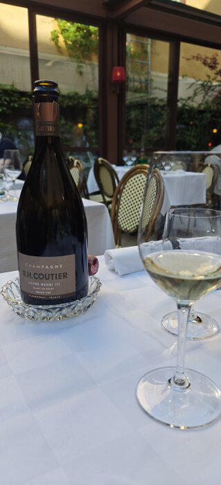 Champagneflaska och vinglas på ett dukat bord i en elegant restaurangmiljö.
