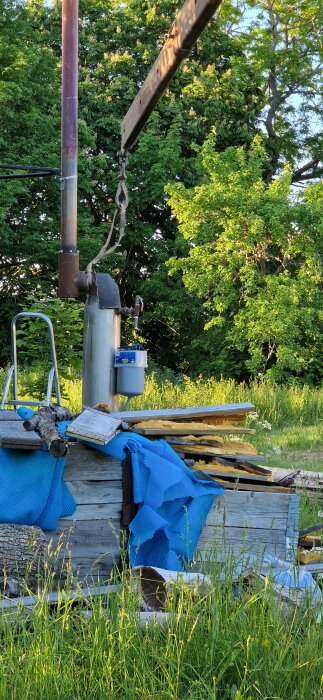 Kamin vid en pool, omgiven av blå täckmaterial och träbitar, med en kran och lyftanordning från gröna faran.