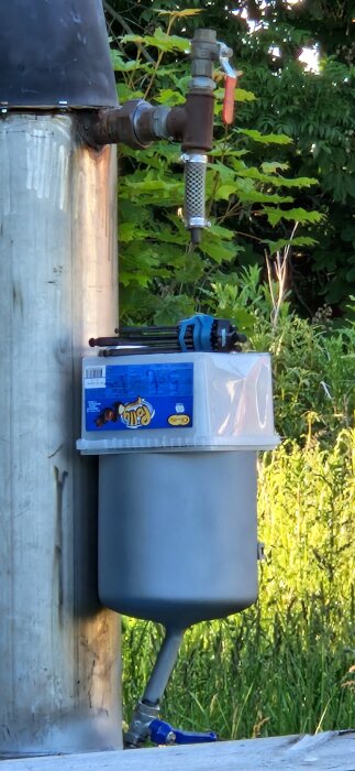 Grå kamin bredvid frodig grönska, med ansluten ventil och blå märkt hink. Makita-verktyg placerad ovanpå.