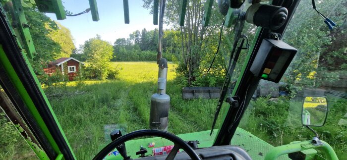 En grön traktor sedd inifrån med en kamin på en äng och ett rött hus i bakgrunden, flyttad från garage till poolområde.