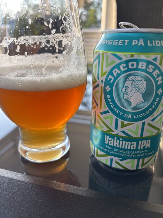 Yakima IPA i glas bredvid en burk Jacobsen Yakima IPA med soligt bakgrundsljus.