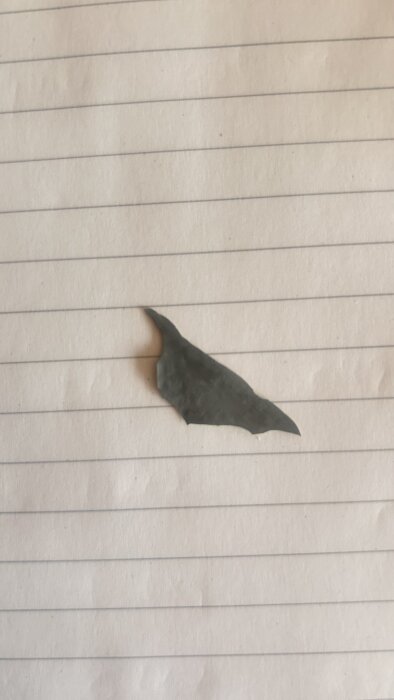 En bit material med grå utsida och gul insida placerad på ett randigt papper.