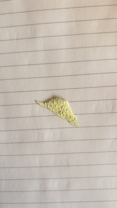 Gult, triangelformat plastfragment ligger på ett linjerat papper.