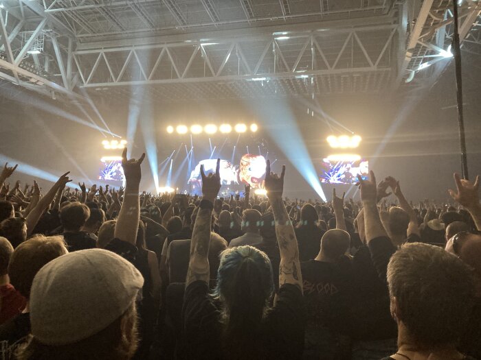 Publik med händer i luften vid en rockkonsert, ljusshow på scenen.