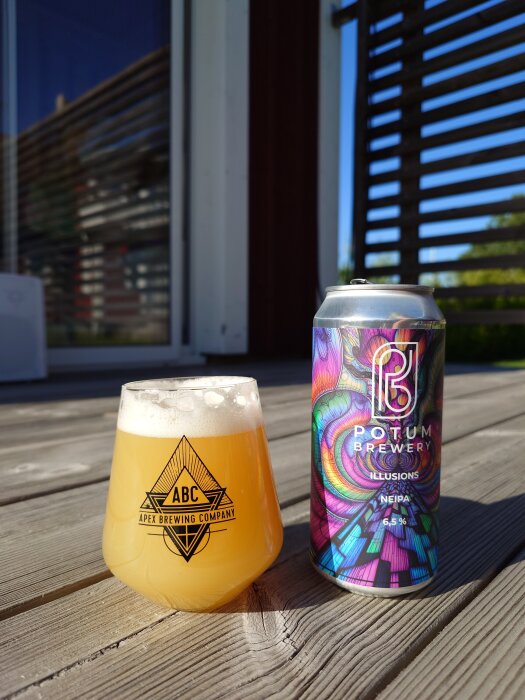 A glass of hazy beer and a colorful Potum Brewery can on a wooden deck in the sun.