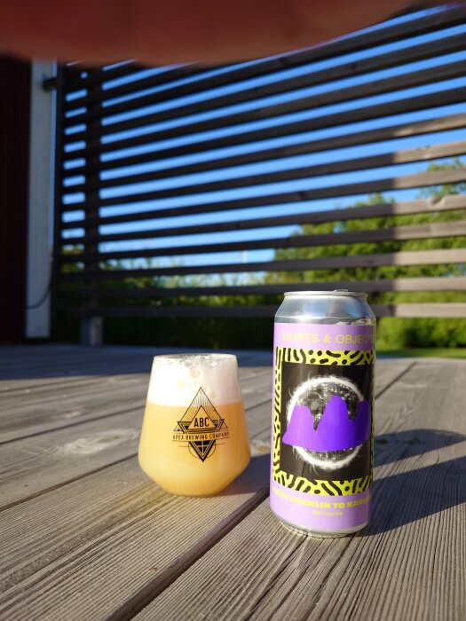 Ett glas öl från Apex Brewing Company och en burk Shapes & Objects IPA på ett trädäck i solskenet.