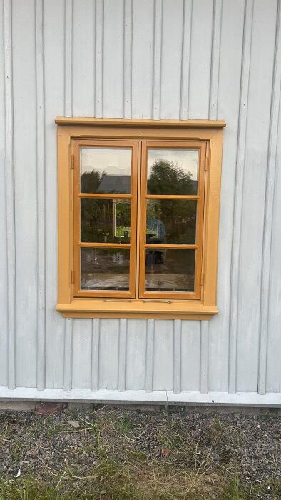 Fönster med orange fönsterkarm mot en ljusgrå trävägg. Reflektioner syns i glaset.