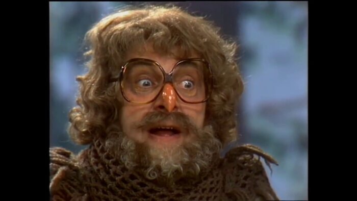 En person med stort hår, glasögon och en falsk näsa gör en förvånad min.