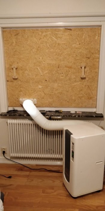 Bärbar AC med slang installerad genom plywoodskiva i fönster.