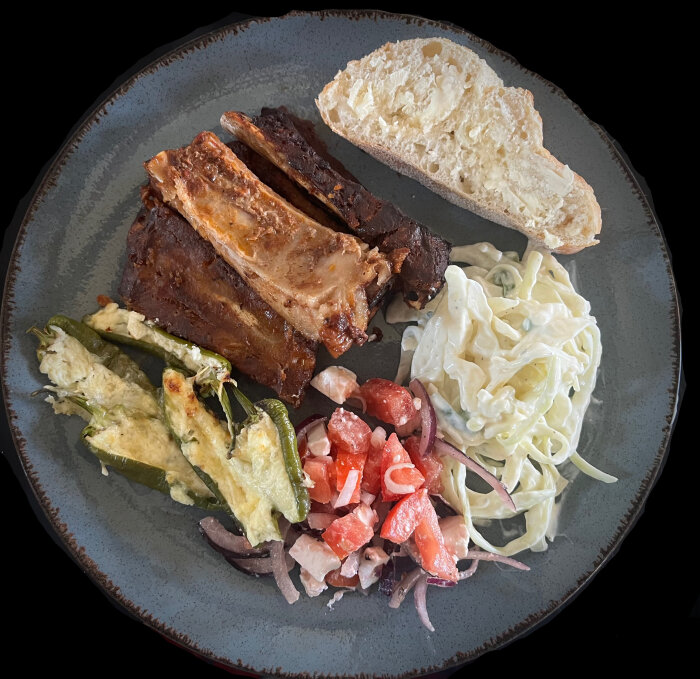 Tallrik med kamben, coleslaw, ugnsstekta fyllda padrones, nybakat bröd och tomat- och fetaostsallad.