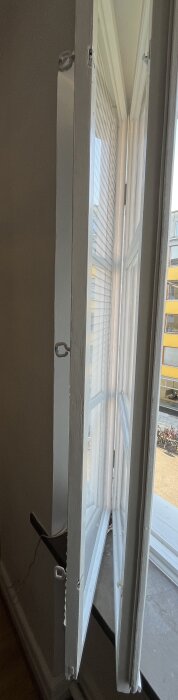 Träfönster med två glasrutor öppnas inåt som en bok, visar insidan av fönstret och utsikt över en livlig gata.