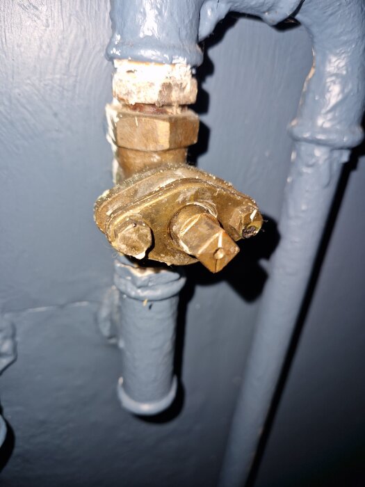 Gammal metallventil monterad på en blåmålad väggansluten ledning, använd för vattenflödesreglering till en radiator i ett garage.