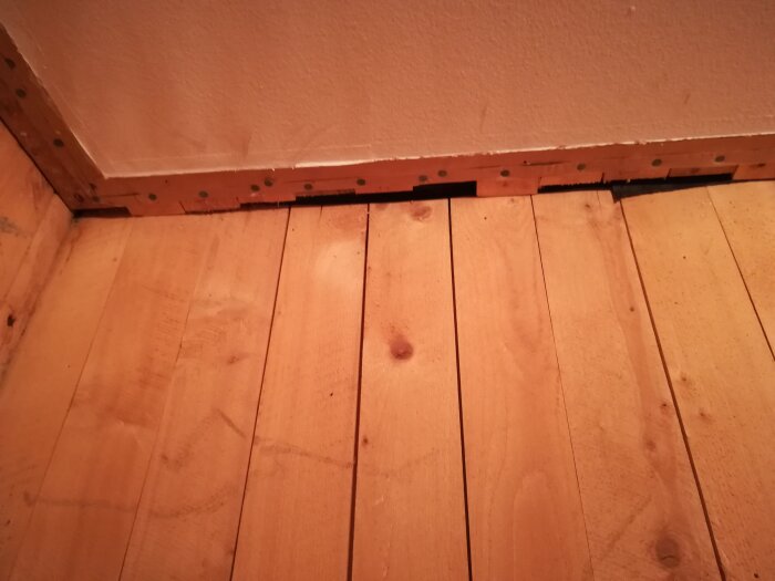 En närbild av ett innertak och vägg hörn med träpanel och ett svart material synligt ovanför panelen.