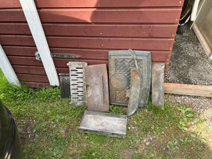 Rostiga delar från en Jøtul vedeldad kamin ligger på marken utanför ett rödbrunt förråd.