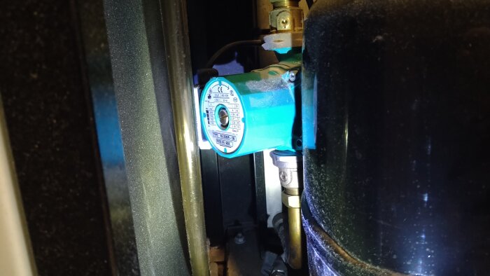 En cirkulationspump av metall i närbild, del av ett uppvärmningssystem, med etikett och anslutna rör.
