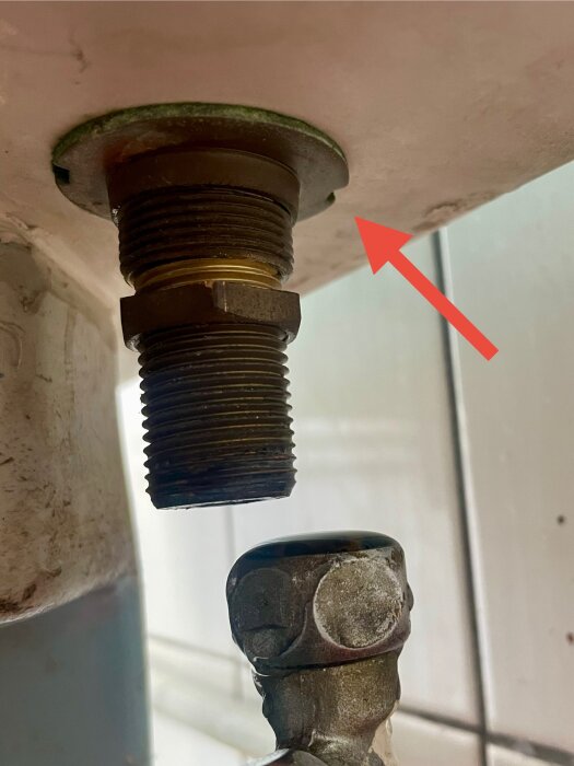 Gammal toalettventil underifrån med ett rör gängat i ett annat rör, röd pil pekar på skarven.